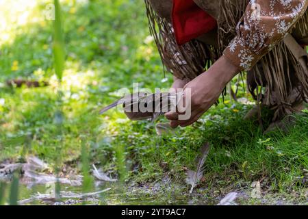 Ein Mann in indischer Kleidung pflückt eine Vogelfeder auf einer Wiese am Ufer eines Baches Stockfoto