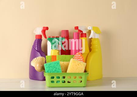 Verschiedene Reinigungsmittel und Verbrauchsmaterialien auf weißem Marmortisch vor beigefarbenem Hintergrund Stockfoto