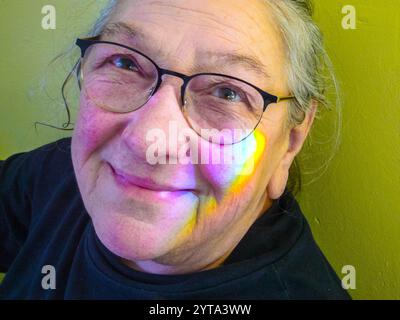Eine ältere Frau, eine Verzweiflung der Siebenbürger Sachsen, blickt mit einem strahlenden Lächeln und einem Regenbogen, der auf ihre Wange scheint, während sie in ihr sitzt Stockfoto