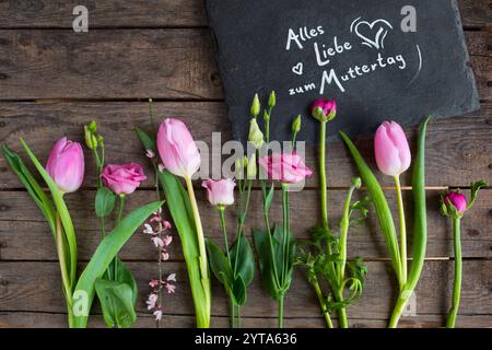 Liebevolle Müttertagsgrüße mit Frühlingsblumen und Text auf einem Schieferteller mit rustikalem Holzhintergrund Stockfoto