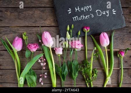 Liebevolle Müttertagsgrüße mit Frühlingsblumen und Text auf einem Schieferteller mit rustikalem Holzhintergrund Stockfoto