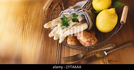 Saisonaler frischer weißer Spargel. Frühlingsgemüse mit Zutaten für ein Menü in einem Korb auf rustikalem Holz. Sonnige Küchenszene für ein gesundes Gastronomie-Konzept im Frühjahr. Stockfoto