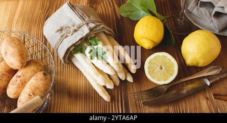 Saisonaler frischer weißer Spargel. Frühlingsgemüse mit Zutaten für eine Speisekarte auf Holz. Sonnige Küchenszene für ein gesundes Gastronomiekonzept im Frühling. Stockfoto