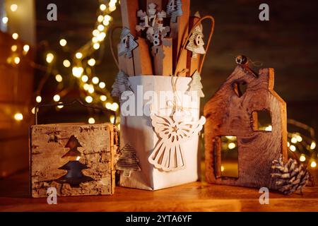 Weihnachtsdekoration mit handgefertigtem Adventskalender. Kleine Pappschachteln in Papiertüte, verziert mit einer Lichterkette auf rustikalem Holzhintergrund. Umweltfreundliche weihnachtsverpackung. Stockfoto