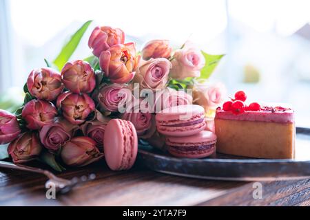 Schöner rosafarbener Blumenstrauß und feine Köstlichkeiten. Süßes Gebäck mit Rosen und Tulpen vor verschwommenem hellem Hintergrund. Konzept für Hochzeit und Muttertag. Stockfoto