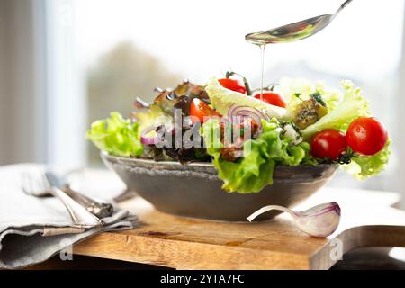 Farbenfroher Salat mit frischen Zutaten, zubereitet mit einem Löffel Olivenöl in einer Keramikschale. Gesundes Nährstoffkonzept für Fitness und Frühlingsdiät. Stockfoto