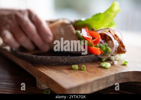 Hand reicht für Tortilla-Wrap mit frischen Gemüse und gebratenem Hähnchenfleisch auf Teller. Hintergrund für gesunden Snack mit kurzer Schärfentiefe. Stockfoto