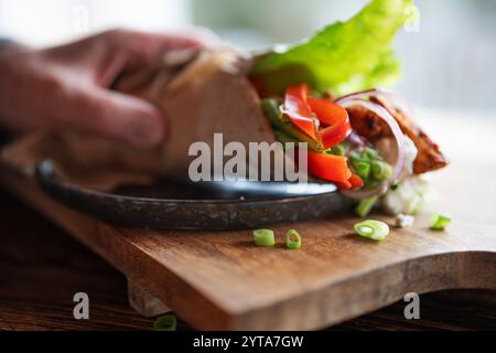 Hand reicht für Tortilla-Wrap mit frischen Gemüse und gebratenem Hähnchenfleisch auf Teller. Hintergrund für gesunden Snack mit kurzer Schärfentiefe. Stockfoto