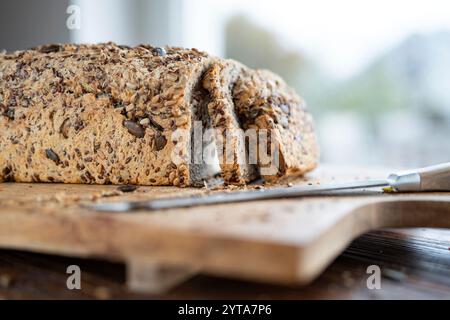 Frisch geschnittenes Mehrkornbrot auf Holzoberfläche mit einem Kniffe. Nahaufnahme vor einem hellen Fenster. Stockfoto