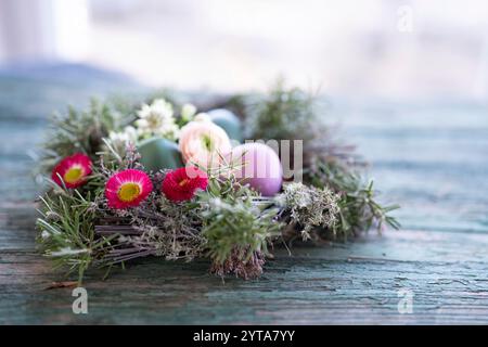 Bunte ostereier in einem Kräuternest mit Frühlingsblumen auf verwittertem rustikalen Holztisch. Hintergrund mit kurzer Feldtiefe und Platz für Text. Stockfoto