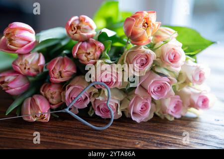 Wunderschöner Blumenstrauß aus rosa Rosen und Tulpen mit Herzform auf dunklem Holz für Muttertagsgrüße. Stockfoto