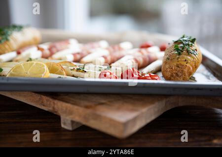 Gebratener weißer Spargel, in Speck gewickelt, mit Kräuterkartoffeln und Tomaten auf Backblech. Nahaufnahme mit kurzer Schärfentiefe. Stockfoto