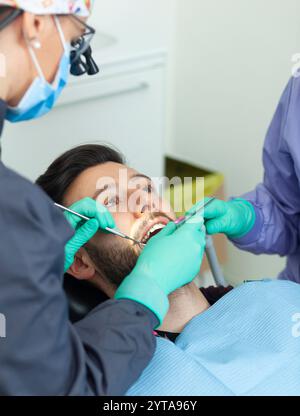 Eine Zahnärztin untersucht in einer Zahnarztpraxis einen männlichen Patienten mit professionellen Werkzeugen und persönlicher Schutzausrüstung Stockfoto