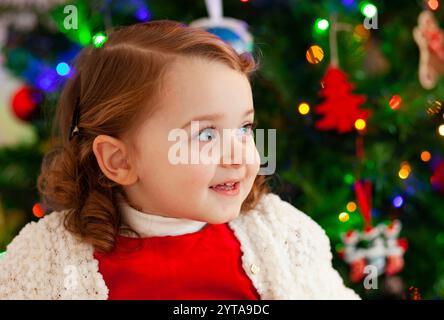 Porträt eines schönen kleinen Kindes mit rotem Kleid in der Nähe des Weihnachtsbaums Stockfoto