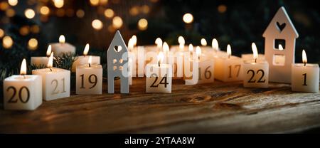 Adventskalender aus 24 brennenden Kerzen, verziert auf dunklem Holz mit goldenem Bokeh. Weihnachtshintergrund mit Platz für Text. Nahaufnahme. Stockfoto