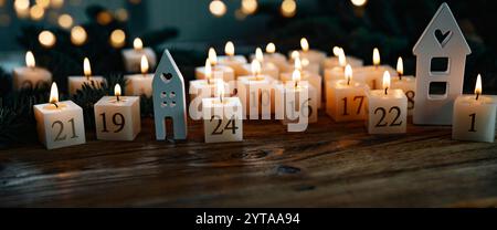 Adventskalender aus 24 brennenden Kerzen, verziert auf dunklem Holz mit goldenem Bokeh. Weihnachtshintergrund mit Platz für Text. Nahaufnahme. Stockfoto