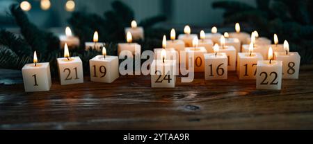 Adventskalender aus 24 brennenden Kerzen. Hausgemacht aus Bienenwachs und nachhaltig auf dunklem rustikalem Holz dekoriert. Weihnachtshintergrund mit goldenem Bokeh für Grüße und Platz für Text. Stockfoto