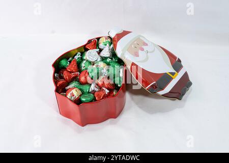 Eine Weihnachtsdose in Form des Weihnachtsmanns enthält eingewickelte Schokoladenbonbons. Die Oberseite wurde entfernt und zeigt eine Dose voller eingewickelter Süßigkeiten. Stockfoto