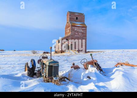 Ein alter Traktor sitzt im Schnee neben einem Getreidesilo. Die Szene ist ruhig und friedlich, der Schnee bedeckt den Boden und die alte Farm-Ausrüstung Stockfoto