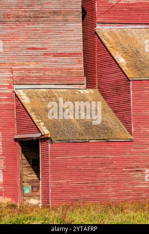 Eine rote Scheune mit einer Tür und einem Dach. Das Dach ist schräg und es fehlen ein paar Schindeln Stockfoto