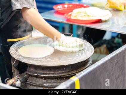 Ein Mann trägt Roti-Teig auf die heiße Pfanne auf, um Roti auf dem Straßenmarkt zu machen. Stockfoto