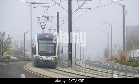 Bellevue, WA, USA - 4. Dezember 2024; Sound Transit Link Stadtbahn im Nebel auf geteilter Straße mit Lichtern und Oberleitungen Stockfoto