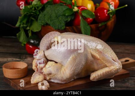 Frisches ganzes Huhn auf hölzernem Schneidebrett mit lebhaftem Gemüse im Hintergrund Stockfoto