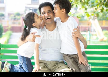 Junge indische Sohn und Tochter küssen Vater, während sie auf der Parkbank sitzen. Binding- und Beziehungskonzept Stockfoto