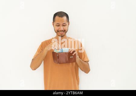 Junge Männer, die ein orangefarbenes Hemd tragen, zeigen Brieftasche und Geld isolierten weißen Hintergrund Stockfoto