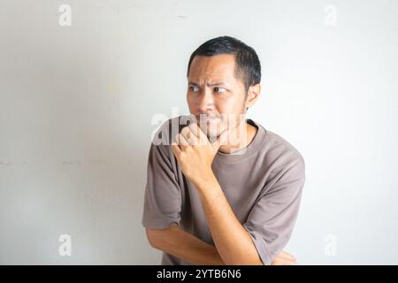 Junger Erwachsener bärtiger asiatischer Mann, der ein grünes Flanellhemd trägt und eine denkende Geste zeigt. Hüfte am Kinn Stockfoto