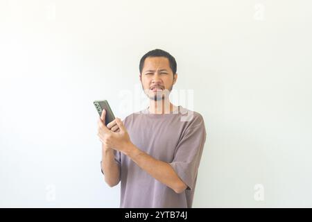 Junge asiatische Männer traurig, während sie ihr Smartphone auf isoliertem Hintergrund halten Stockfoto