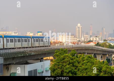 E-Bahnwagen fahren entlang der Strecke im Sky Railway Road Viadukt durch die moderne Stadt mit Gebäuden, Wolkenkratzern und Bäumen Stockfoto