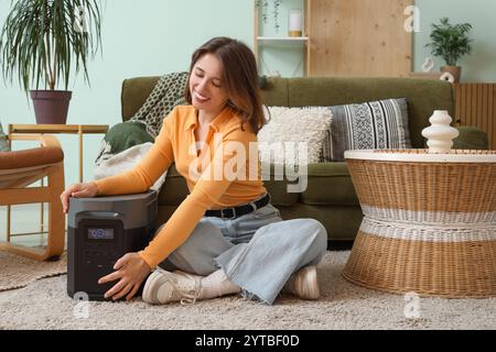 Junge Frau mit tragbarem Kraftwerk zu Hause Stockfoto