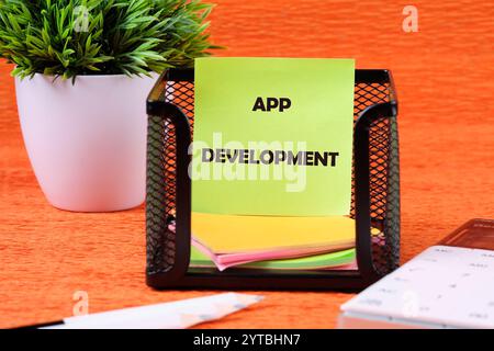 Das Konzept der Technologie und Geschäftsentwicklung. Der Begriff der APP-ENTWICKLUNG ist auf einem grünen Aufkleber in einem Ständer auf orangefarbenem Hintergrund geschrieben. Stockfoto