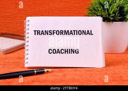 Geschäfts-, Formations- oder Transformationskonzept. Kopierbereich. TRANSFORMIERENDES COACHING auf einem sauberen Notizbuch auf orangefarbenem Hintergrund. Stockfoto