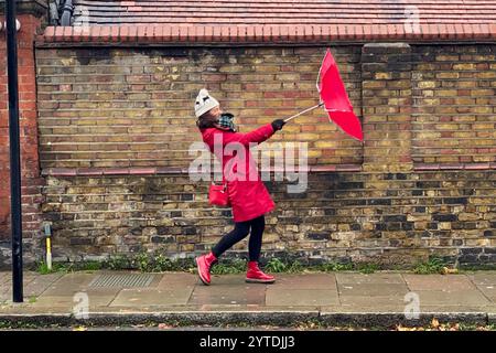 Hammersmith, London, Großbritannien. Dezember 2024. Wetter in Großbritannien: Sturm Darragh bringt Regen und Wind nach Barons Court, London. Im Bild: Raich Keene kämpft unter den Bedingungen mit ihrem Regenschirm. Hinweis: Nidpor/Alamy Live News Stockfoto