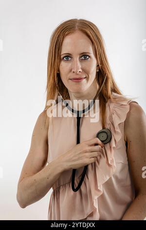Junge Ärztin, in normalen Kleidern gekleidet, hört ihrem Herzen zu. Stockfoto