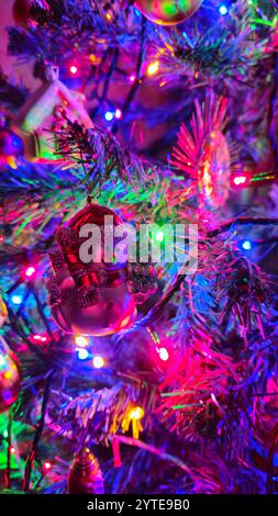 Weihnachtsbaum mit glühenden Girlanden und einem Schneemannspielzeug im Vordergrund, farbenfroher Feiertagshintergrund Stockfoto