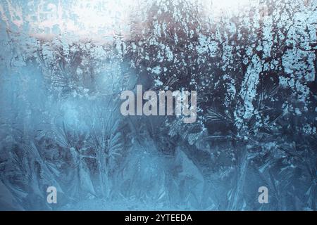Blauer Winterhintergrund mit Frostmuster am Fenster. Wunderschöne frostige Zeichnung. Gefrorenes Fensterglas. Stockfoto