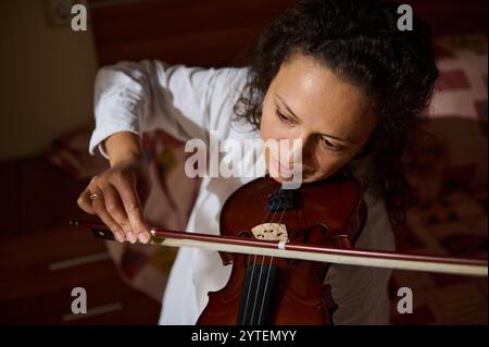 Eine Frau spielt intensiv Geige und zeigt Konzentration und musikalische Leidenschaft in einer warmen, intimen Umgebung. Stockfoto