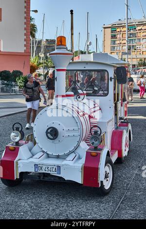 Savona. Italia - 07. Dezember 2024: Ein farbenfroher Touristenzug mit Passagieren parkt auf einem belebten Stadtplatz in Savona, Italien, mit moderner Ausstattung Stockfoto