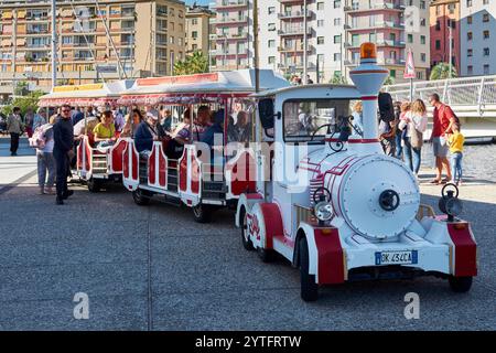 Savona. Italia - 07. Dezember 2024: In Savona, Italien, sitzen die Menschen auf einem pulsierenden Stadtrundfahrt-Zug, der bereit ist, die Sehenswürdigkeiten der Stadt bei Sonnenschein zu erkunden Stockfoto