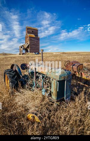 Ein alter blauer Traktor sitzt auf einem Feld mit hohem Gras. Der Traktor ist von vielen Unkraut umgeben und das Feld ist trocken und karg. Die Szene zeigt Stockfoto
