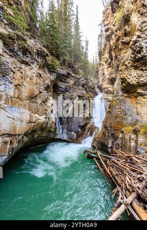 Ein Wasserfall fließt in einen Fluss mit einem großen Holzhaufen am Flussufer. Das Wasser ist klar und die Felsen sind zerklüftet. Die Szene ist friedlich A Stockfoto