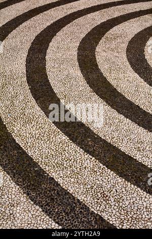 Detailliertes konzentrisches Kreismuster in einem öffentlichen Straßenbelag mit dunklen und hellen Steinen in einem harmonischen Design, ideal für Hintergründe Stockfoto