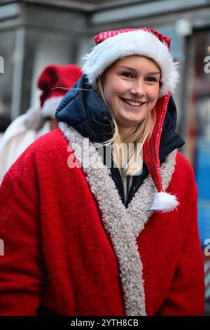 Helsingborg, Skåne, Schweden. Dezember 2024. Weihnachtsmarkt. Leute auf der Straße. Junge Frauen in weihnachtsmannskostümen verteilen Süßigkeiten. Stockfoto