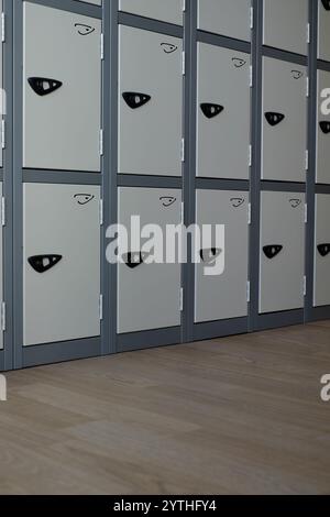 Abschnitt einer Bank grauer Schließfächer mit Kopierraum im unteren Drittel über dem Bodenbelag des Raumes. Stockfoto