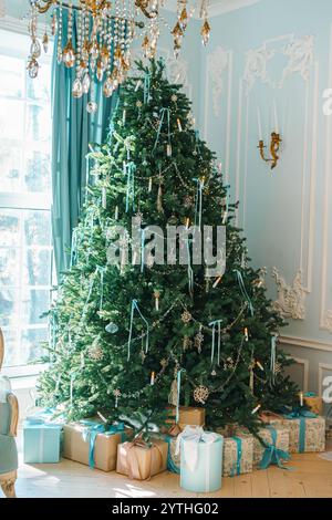 Ein wunderschön dekorierter Weihnachtsbaum steht in einem gemütlichen Raum, geschmückt mit Lichtern und Ornamenten. Darunter warten zahlreiche gewickelte Geschenke, die noch aufwerten Stockfoto