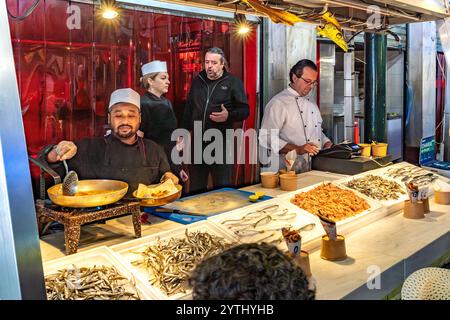 Athen, Attika - GR - 25. Okt. 2024 auf dem Varvakios Central Market frittieren Köche frische Meeresfrüchte, umgeben von Fisch und Garnelen, während die Einheimischen mich engagieren Stockfoto