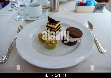 Ein überdachtes Desserttrio mit mehrschichtigem Kuchen mit Schokoladengarnitur, zwei gebackenen Gebäckstücken mit grüner Mandelplatte und einem Eissandwich mit Schokoladenkeks Stockfoto
